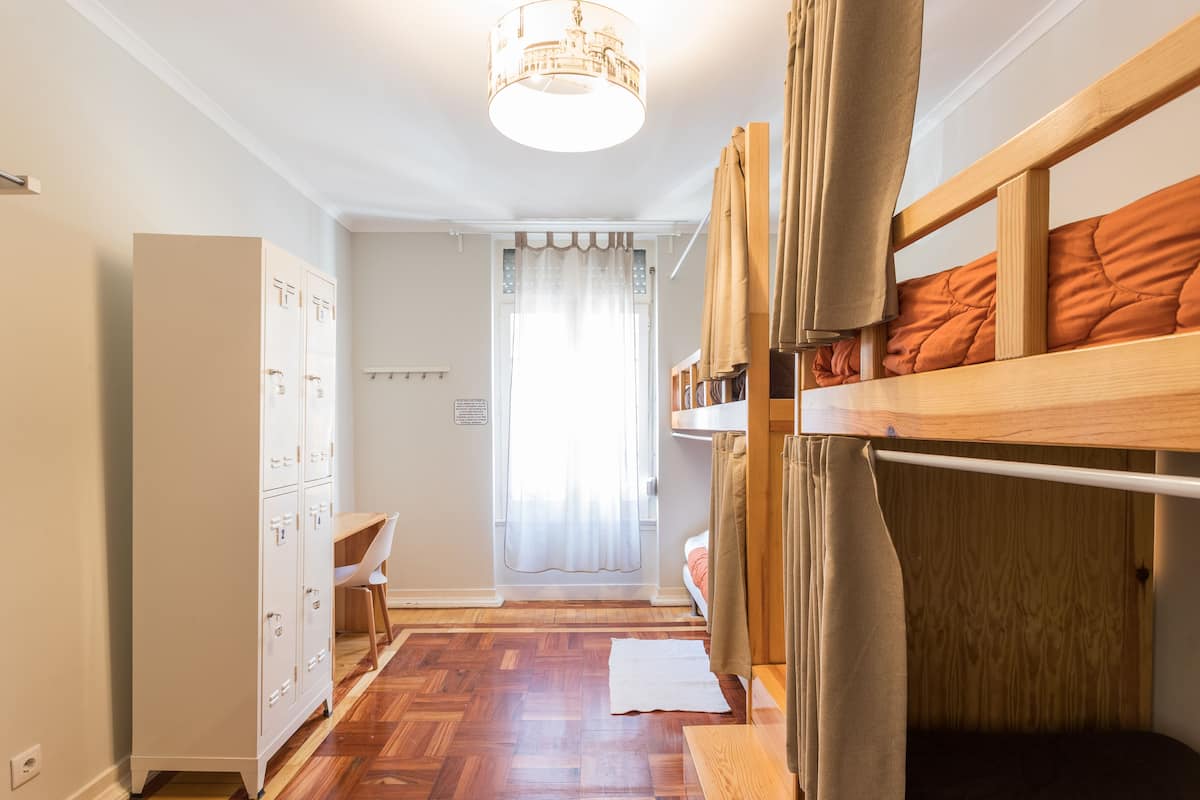 Een studentenkamer met stapelbedden, een bureau, een kledingkast en een raam met gordijnen.