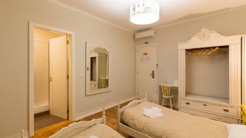A bedroom with two beds, a wardrobe, a mirror, and a door leading to another room.