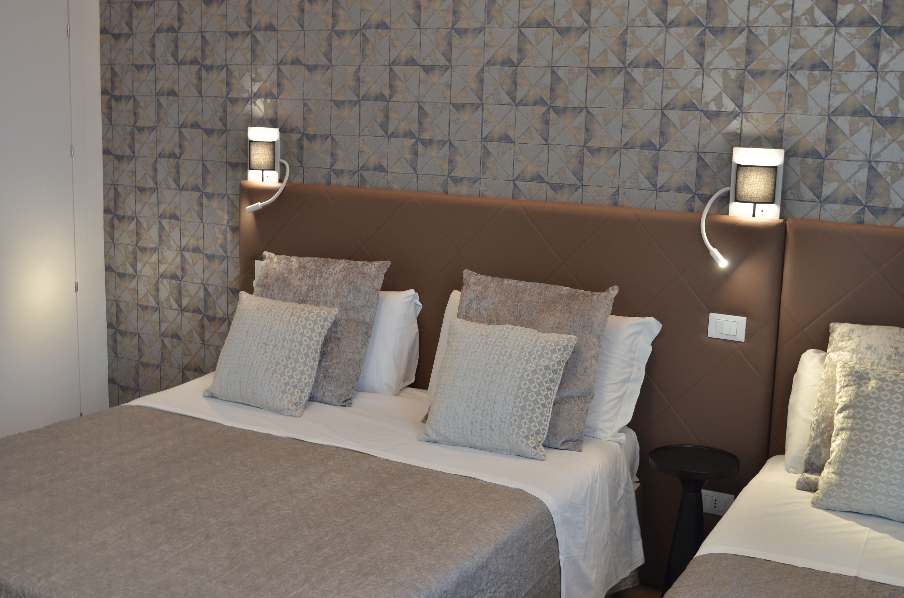 A hotel room with a bed, two bedside tables, and a patterned wall.