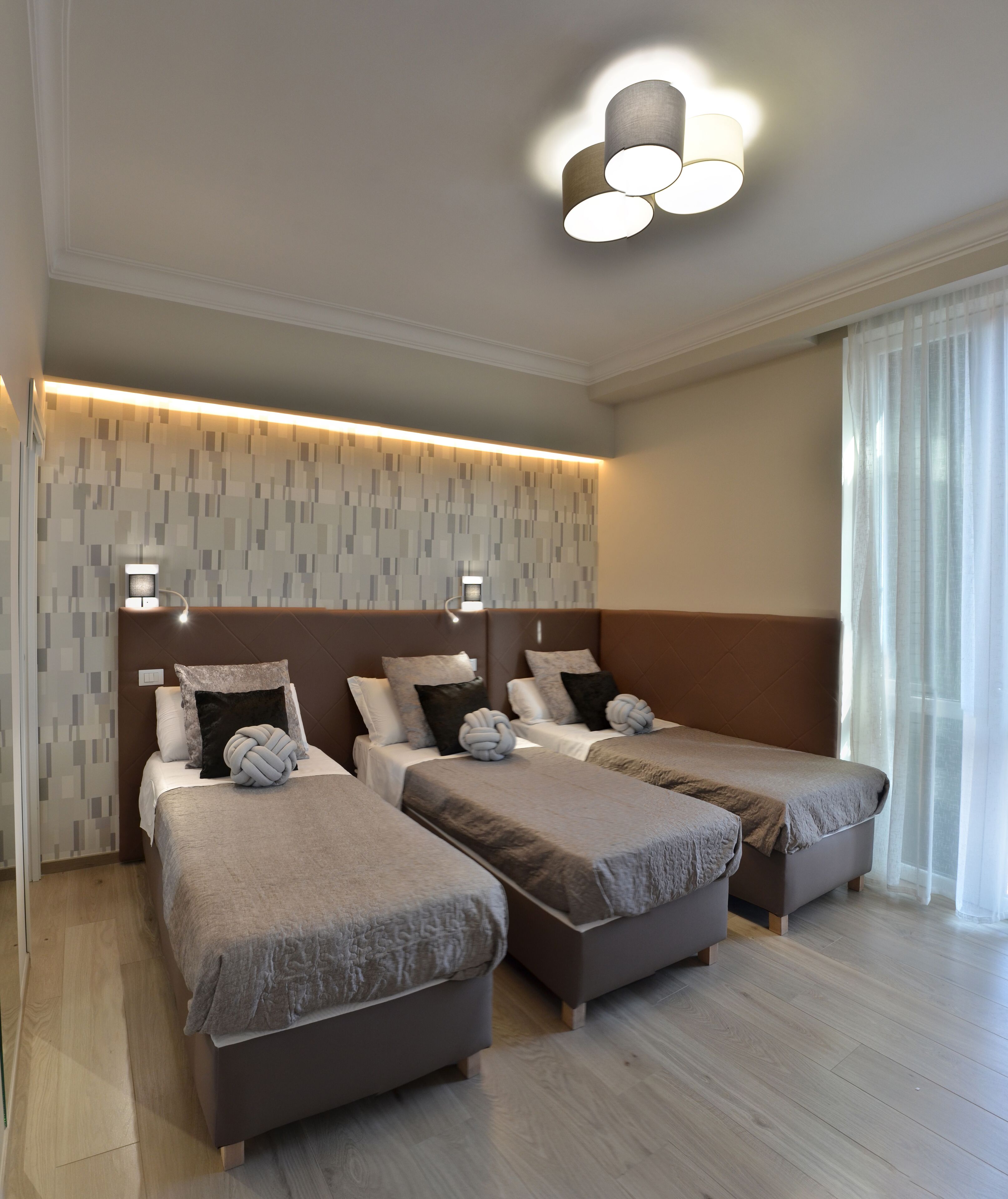 A hotel room with three beds, a patterned wall, and a modern ceiling light fixture.