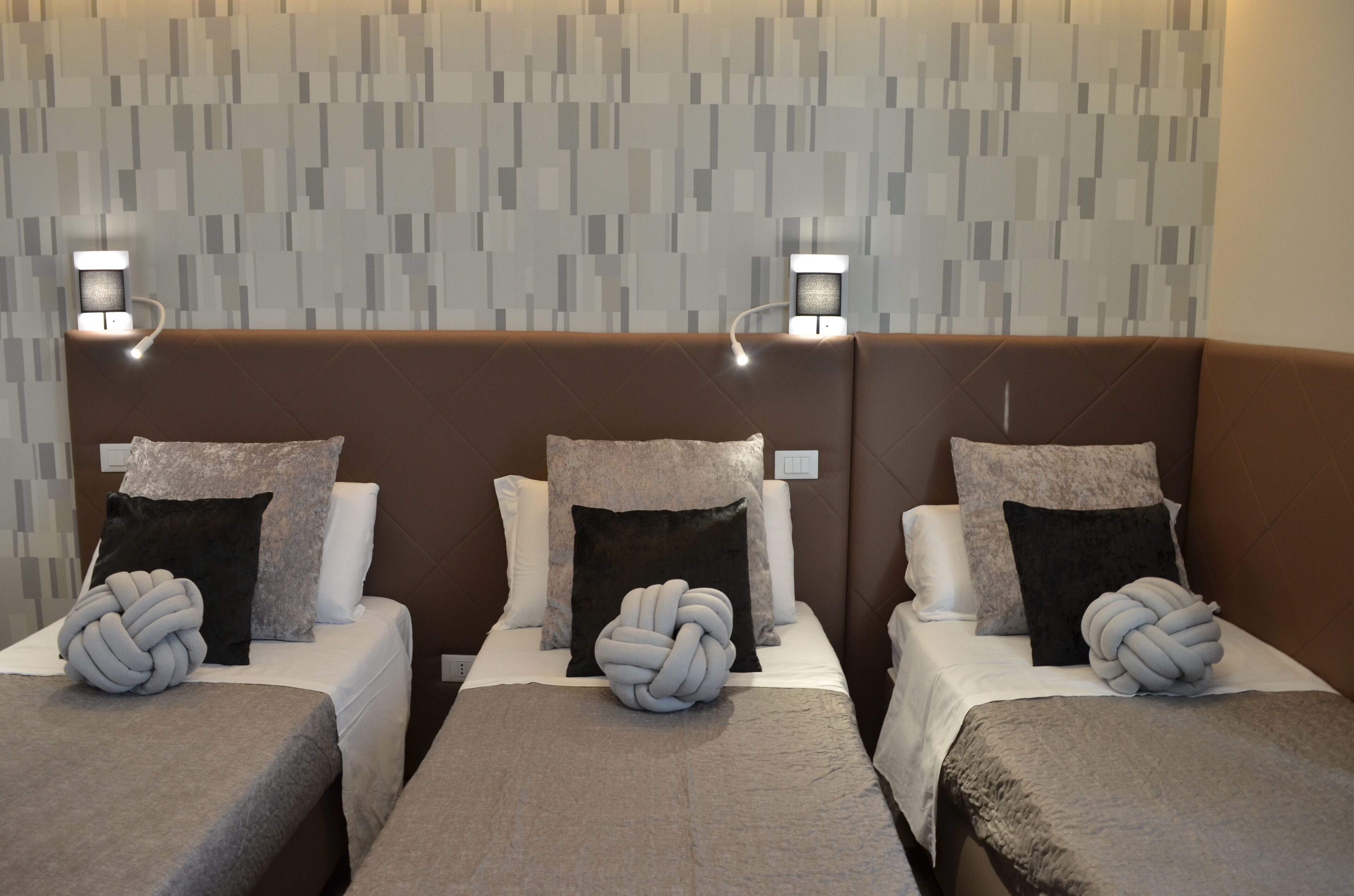A hotel room with three beds, each with a headboard, white linens, and decorative pillows.