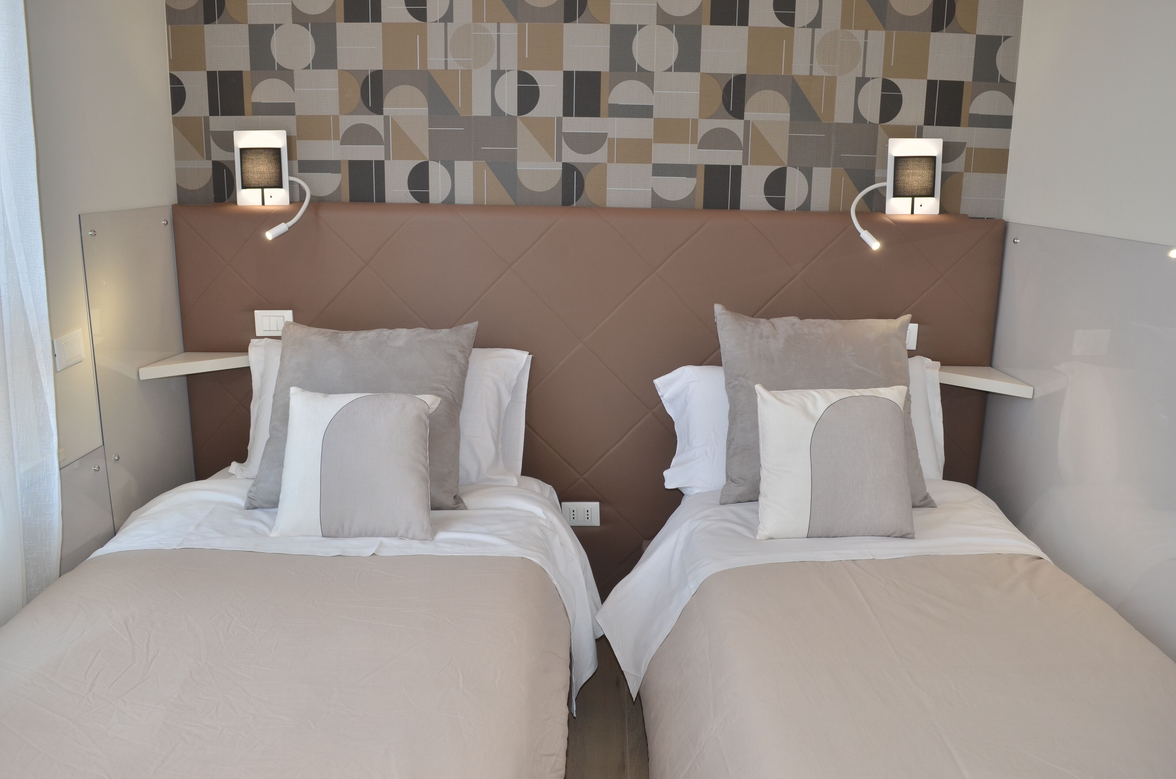 A hotel room with two beds, each with a headboard, bedside tables, and wall-mounted reading lights.