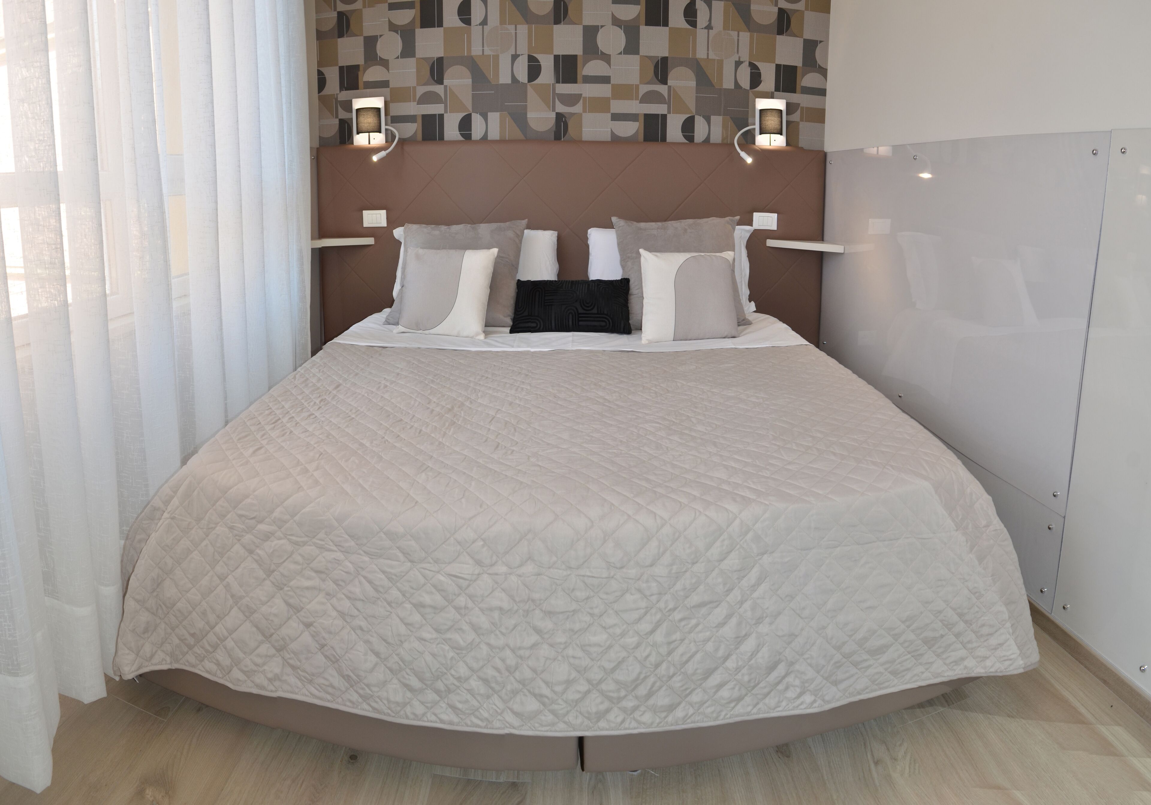Un dormitorio moderno con una cama grande, cabecera con iluminación integrada y pared con estampado geométrico.