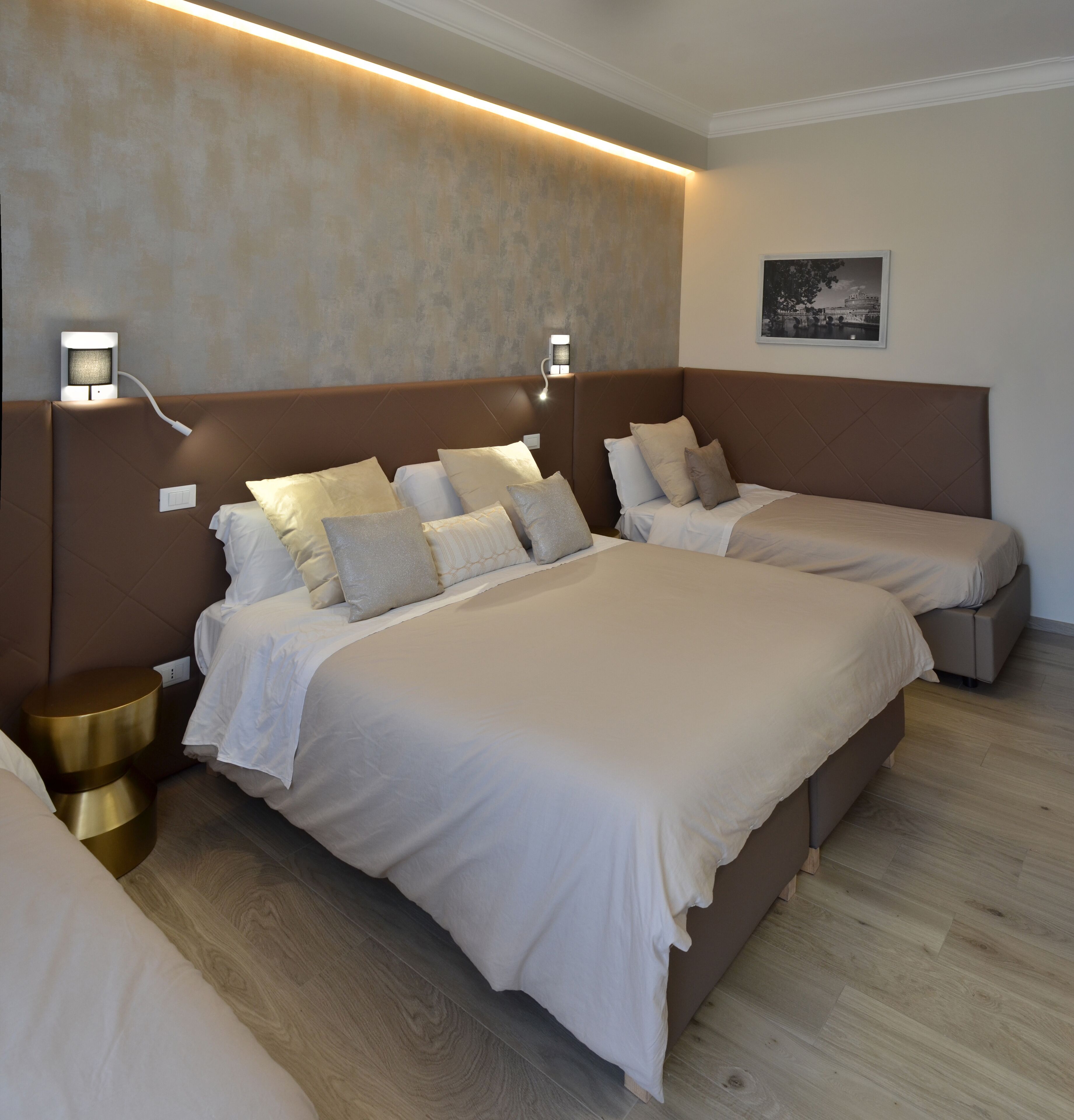 A hotel room with two beds, a nightstand, a wall-mounted lamp, and a framed picture on the wall.