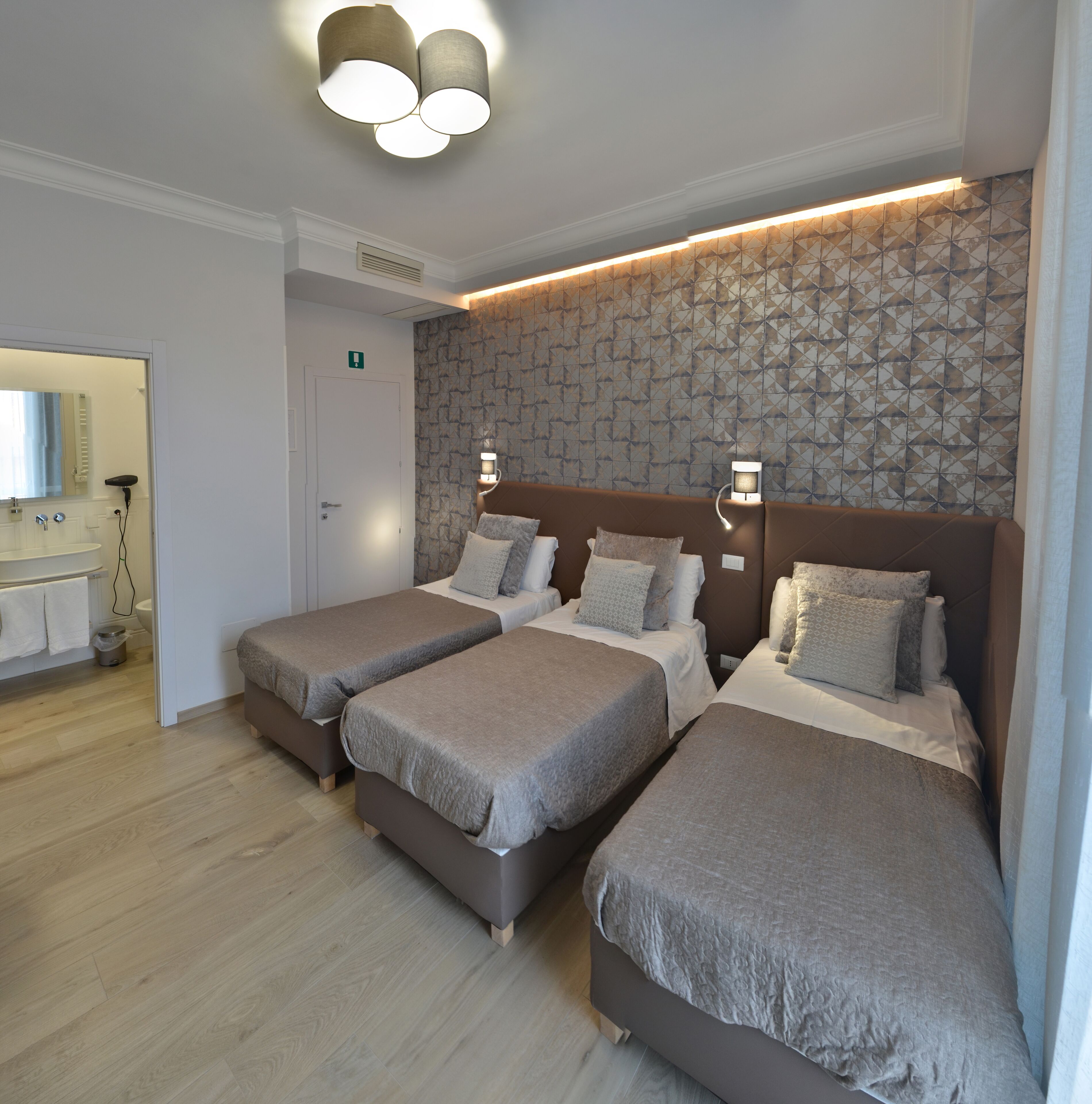 A hotel room with three beds, a bathroom, and a hallway.