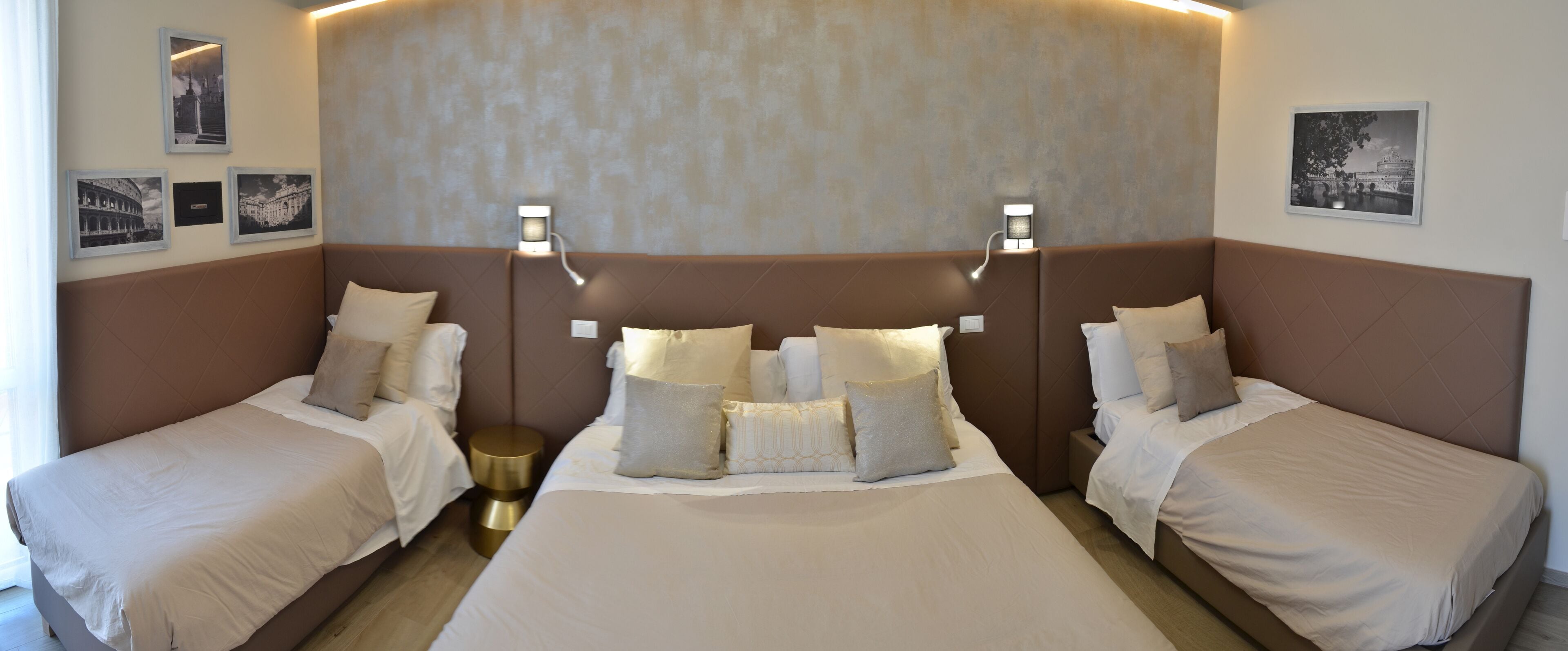 A hotel room with two single beds, a large headboard, and wall-mounted lighting.