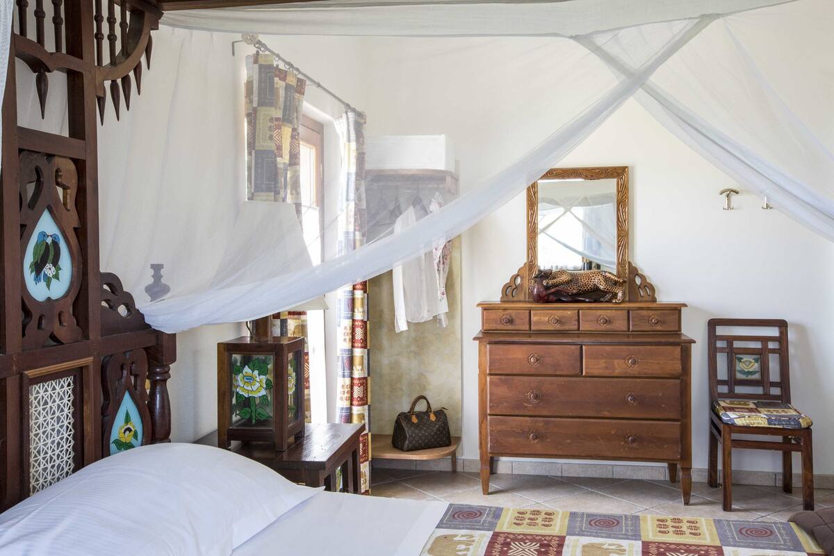 A bedroom with a bed, wooden dresser, chair, and decorative items.
