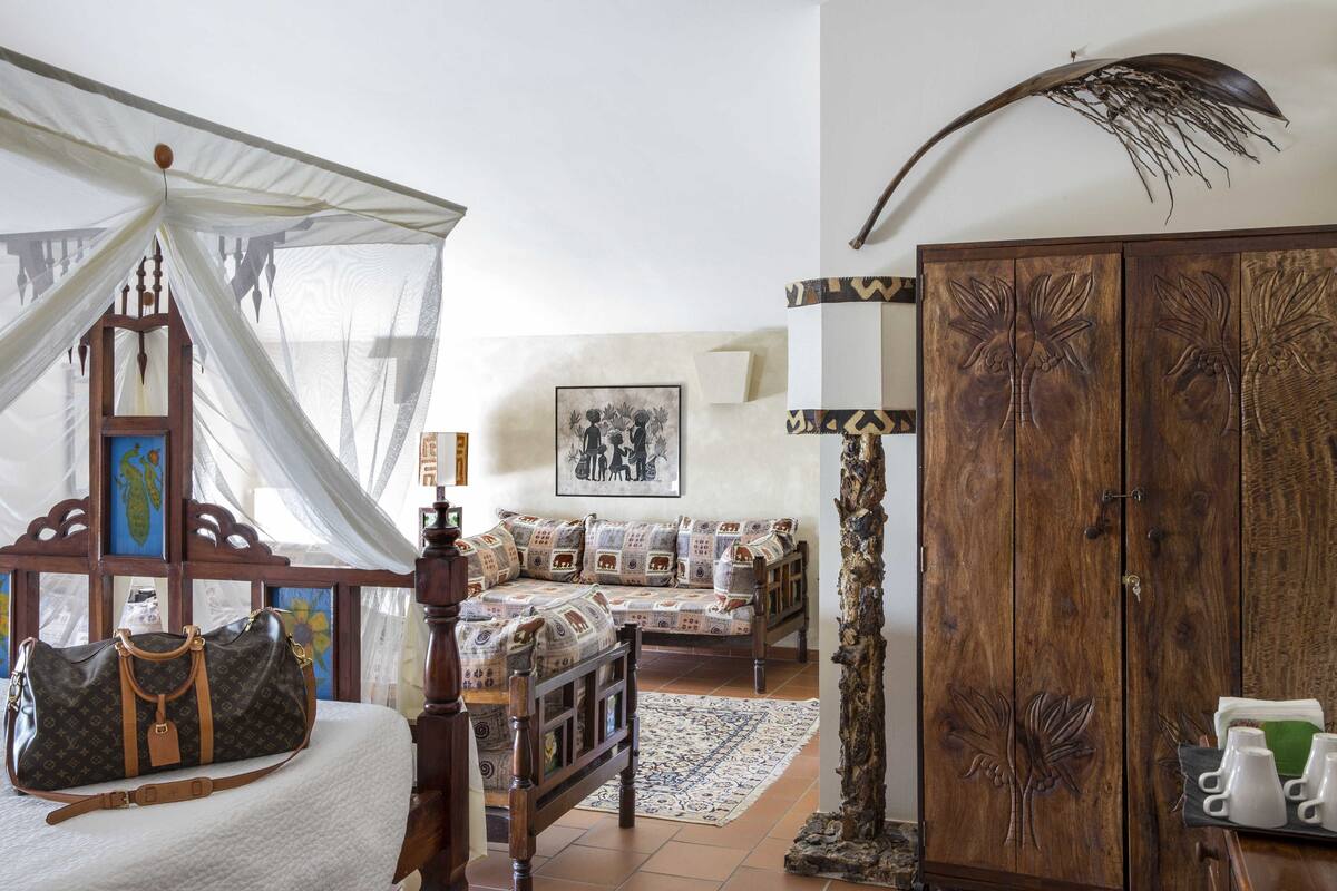 A bedroom with a canopy bed, a wooden wardrobe, and a large decorative piece on the wall.