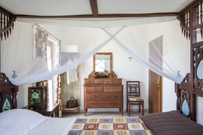 A bedroom with a bed, a wooden dresser, a chair, and a mirror.