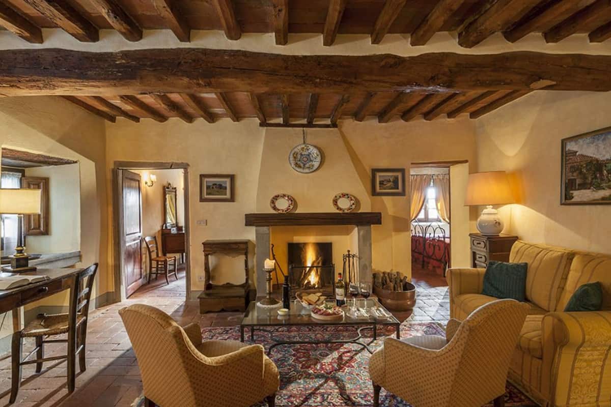 A cozy living room with a fireplace, wooden beams, a dining area, and a sofa.