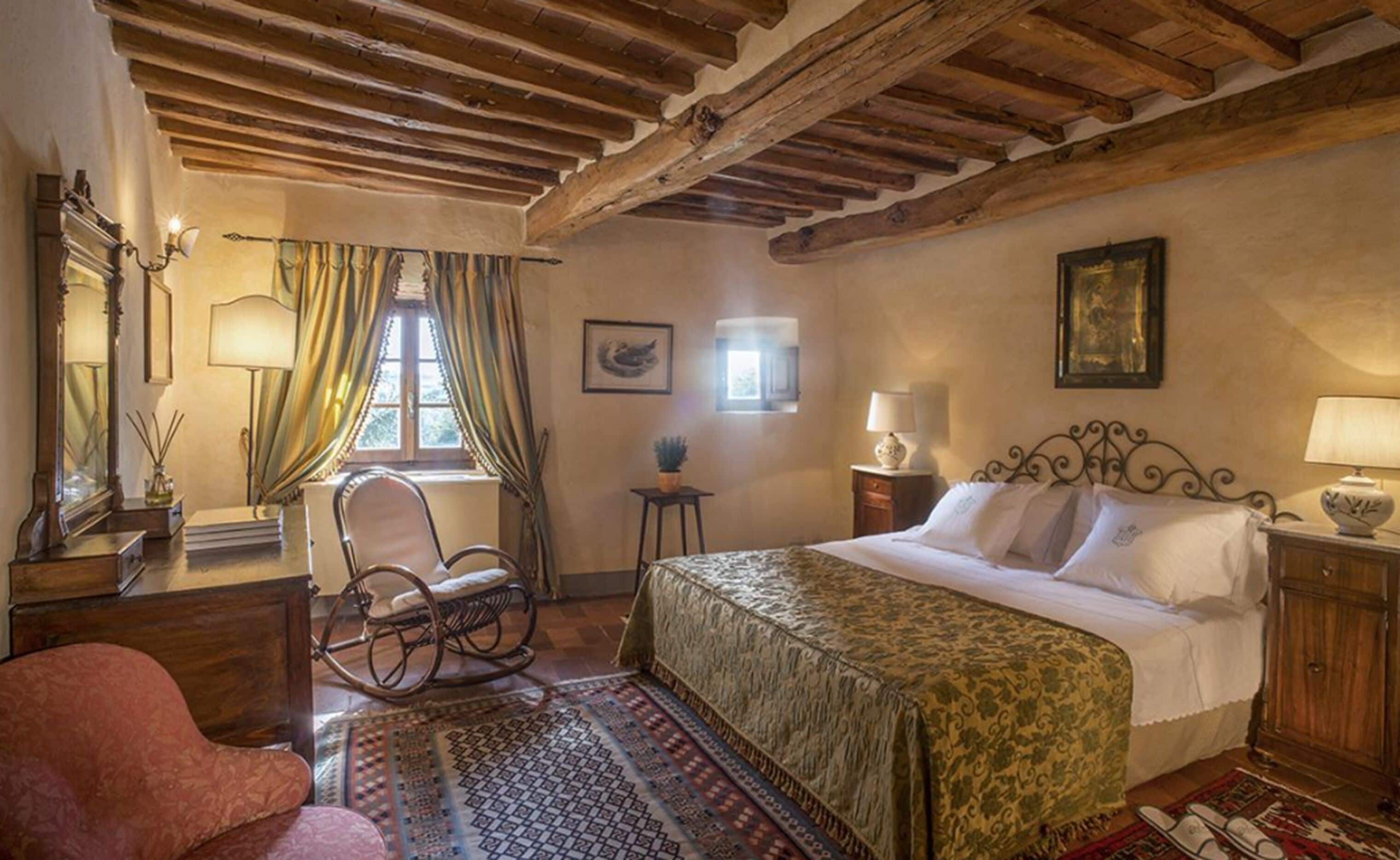A traditional room with a bed, a rocking chair, and a window with curtains.