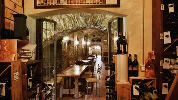 Una bodega con mesas y sillas de madera, estanterías para vino y un arco de piedra.