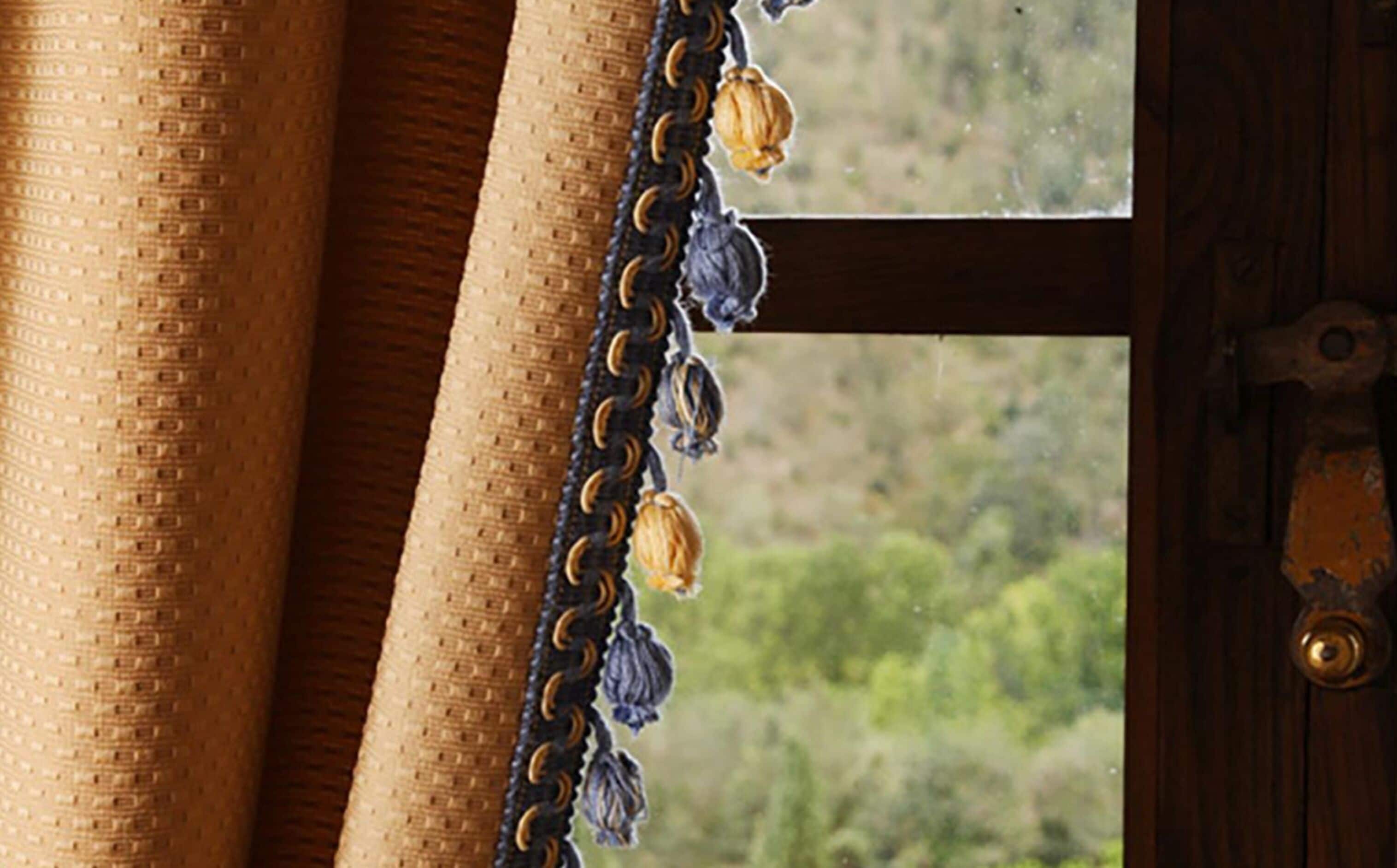 Gros plan sur un tissu texturé, peut-être un rideau, auquel est suspendu un pompon décoratif.
