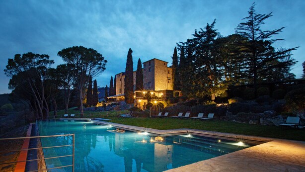A swimming pool with a stone deck, surrounded by trees and a castle-like building in the background. - Castello di Spaltenna- Small Luxury Hotels of the World (Gaiole in Chianti)