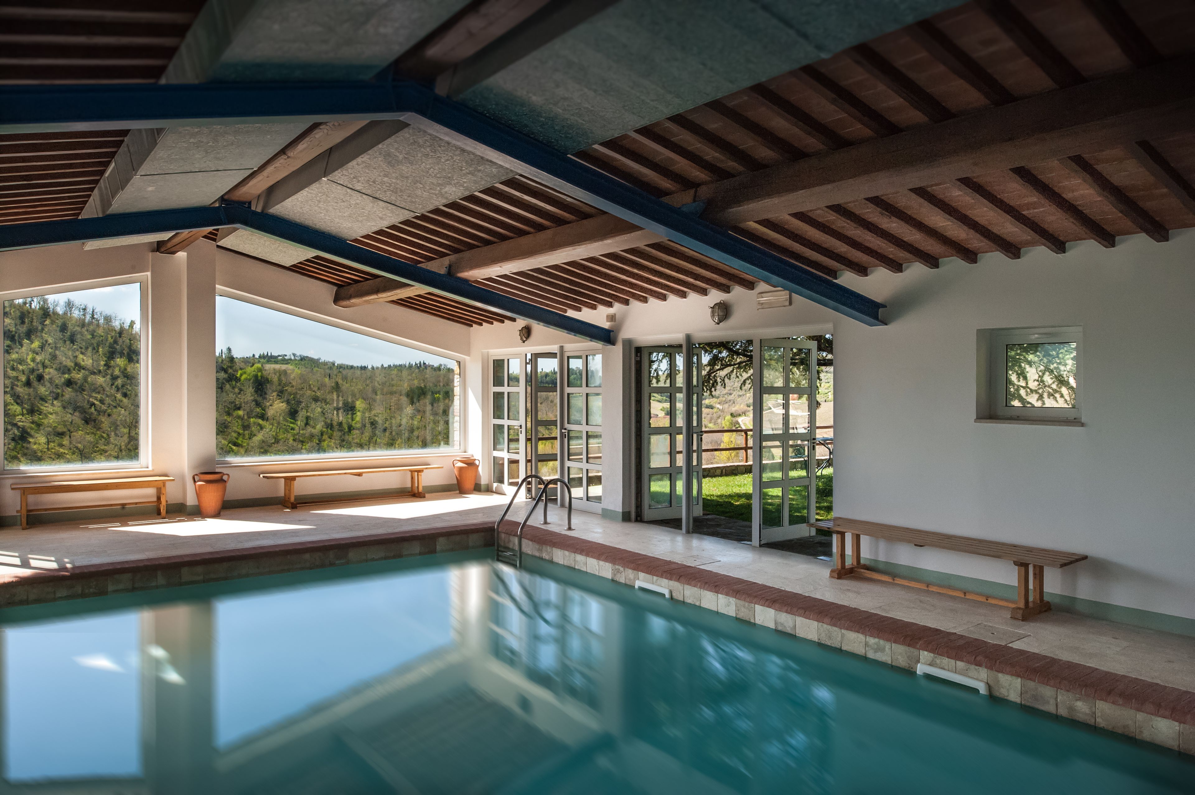 Ein Hallenbad mit Holzbanken und großen Fenstern, die einen Blick ins Freie ermöglichen.