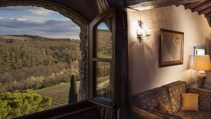 A room with a large window offering a view of a hilly landscape. There is a sofa with patterned upholstery and a lamp on a side table. - Castello di Spaltenna- Small Luxury Hotels of the World (Gaiole in Chianti)