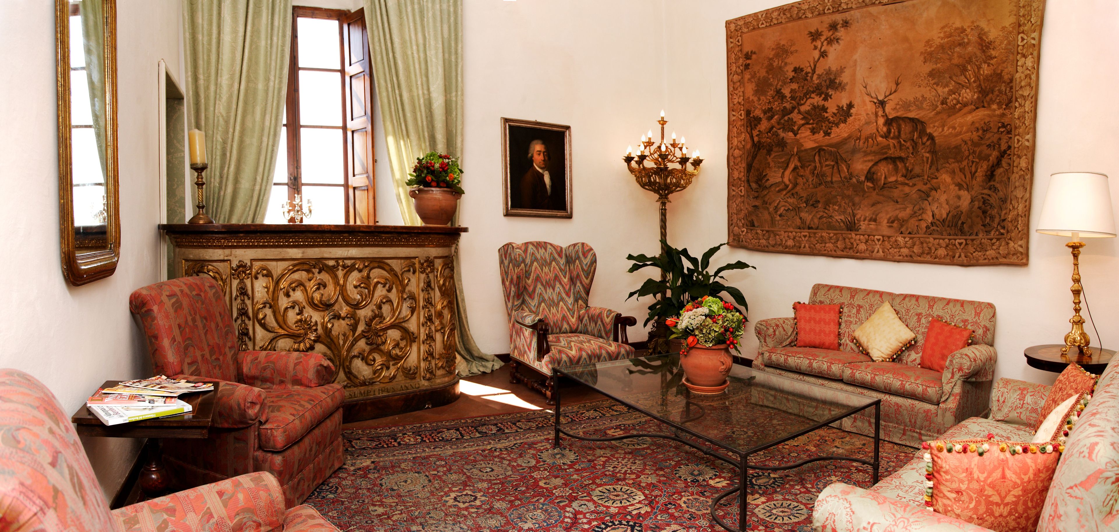 A traditional living room with patterned sofas, a glass coffee table, and a large painting on the wall.