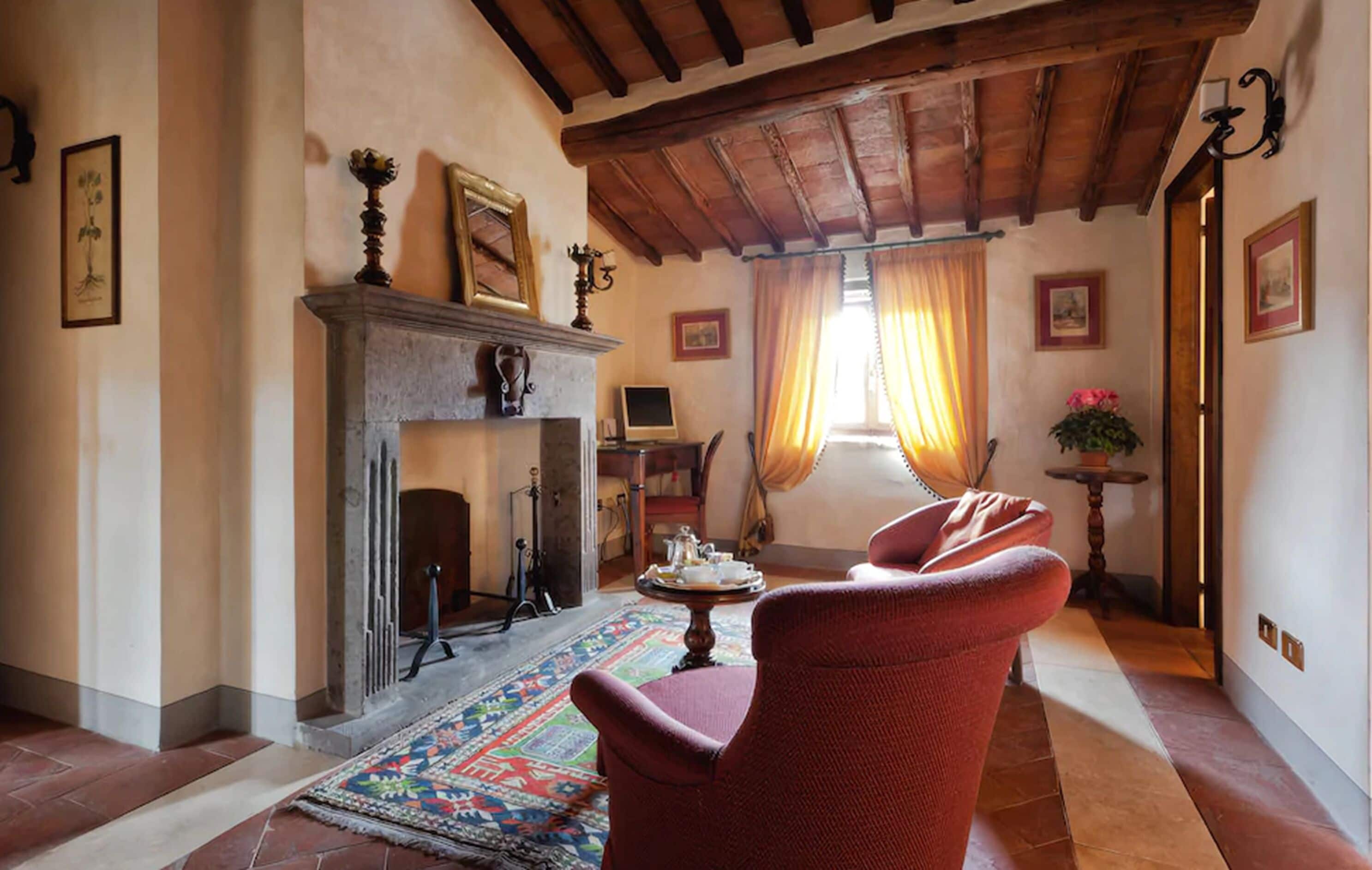 Un salon chaleureux avec une cheminée, des fauteuils rouges, un tapis à motifs et un plafond en bois.