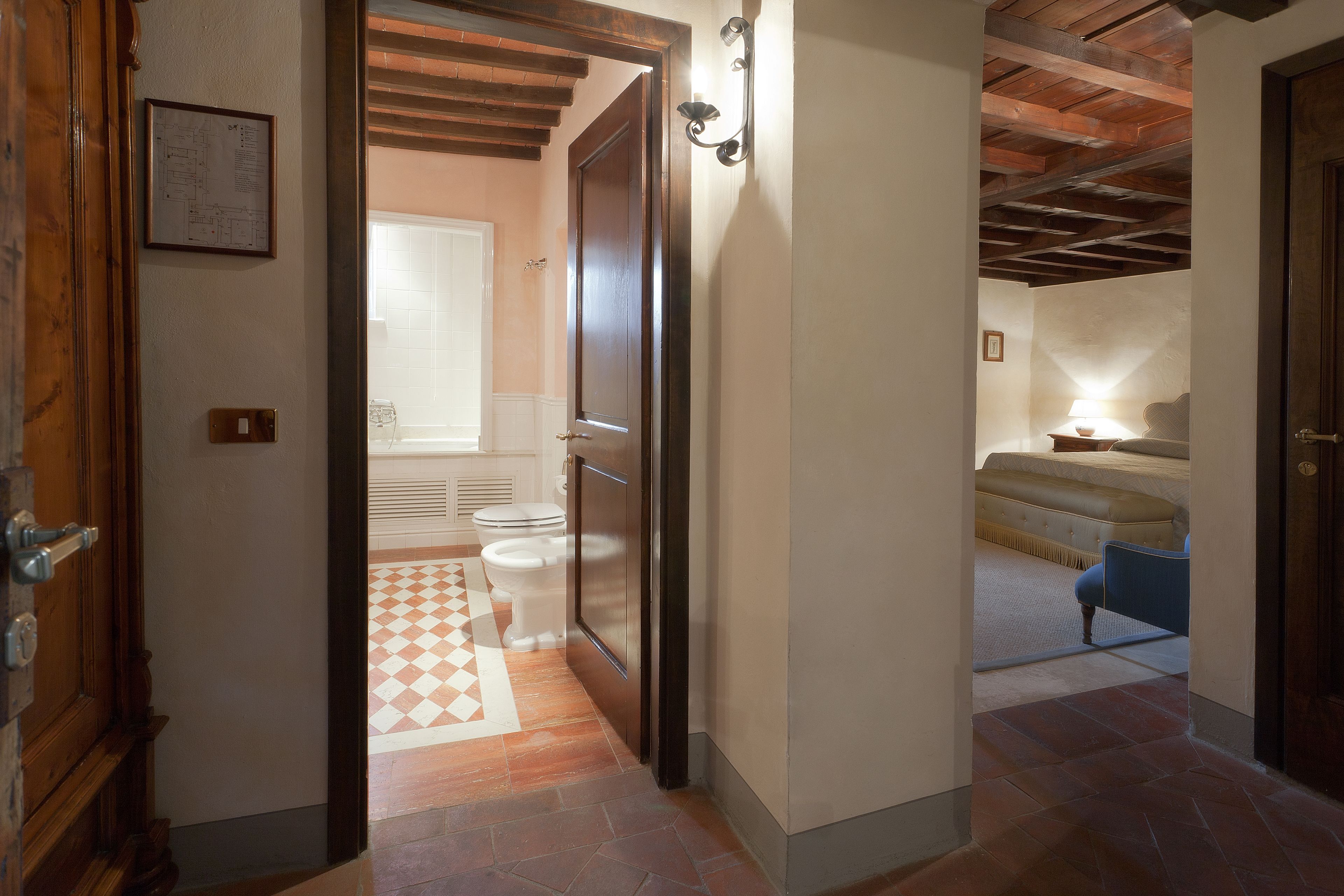A hallway leading to a bathroom with a checkered floor, a toilet, and a shower area.