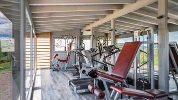 Un gimnasio con equipo de ejercicio, una silla roja y vistas a un viñedo.