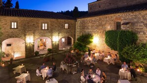 An outdoor dining area with stone buildings and a tower, illuminated by ambient lighting. - Castello di Spaltenna- Small Luxury Hotels of the World (Gaiole in Chianti)