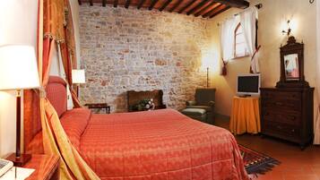 Un dormitorio con pared de piedra, cama con colcha roja, cómoda de madera, televisor y lámpara.