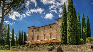 A stone building with a garden, tall trees, and a clear blue sky. - Castello di Spaltenna- Small Luxury Hotels of the World (Gaiole in Chianti)