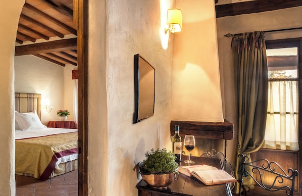 Une pièce chaleureuse avec un lit, une table sur laquelle se trouve un livre, une bouteille de vin et une plante.