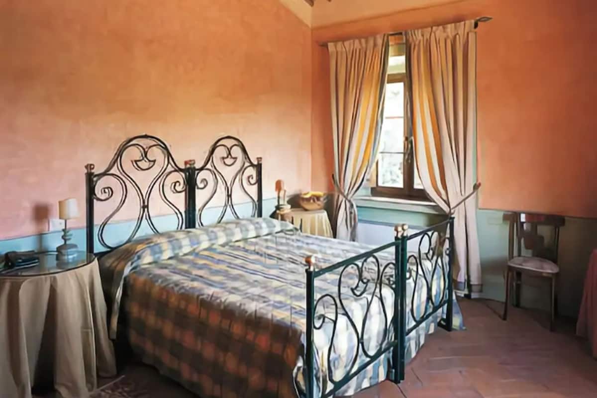 A bedroom with a bed, a small table, a chair, and a window with curtains.