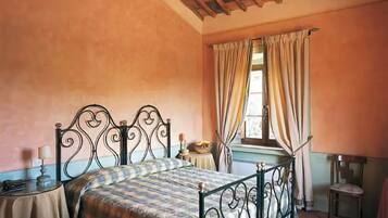 Une chambre à coucher avec un lit, une petite table, une chaise et une fenêtre avec des rideaux.