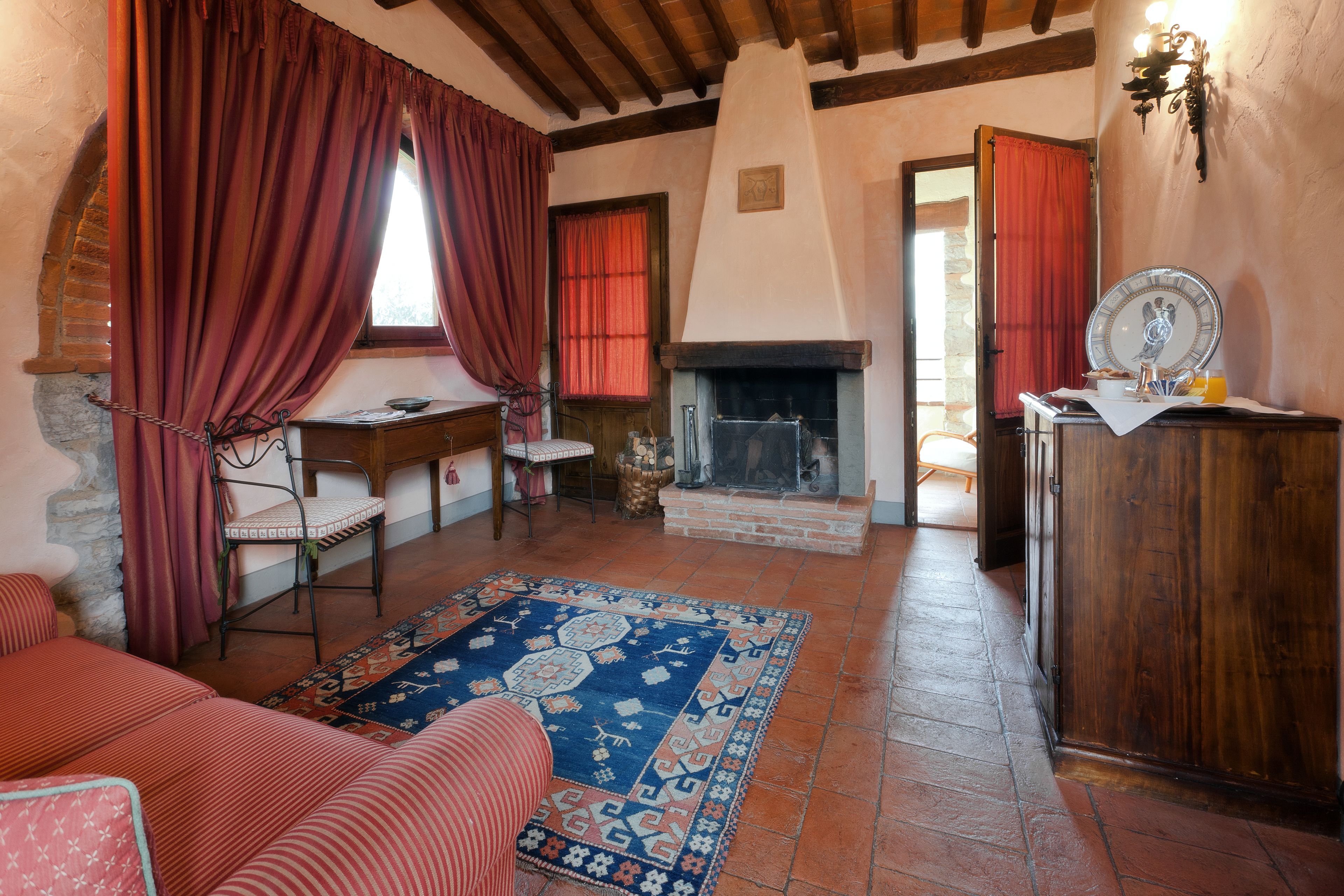 A cozy room with a fireplace, a wooden desk, a chair, a sofa, and a patterned rug.