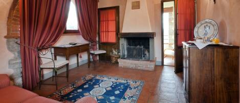 A cozy room with a fireplace, a wooden desk, a chair, a sofa, and a patterned rug.