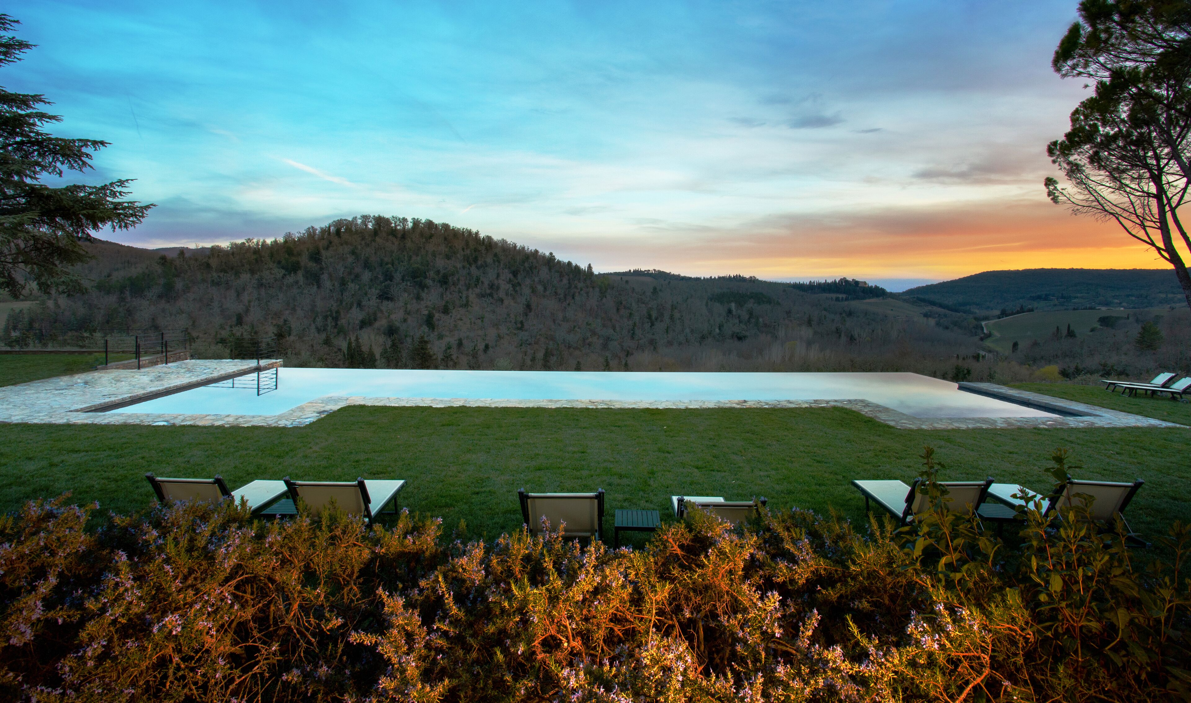 A rectangular pool with a stone border, surrounded by a grassy area with several lounge chairs.