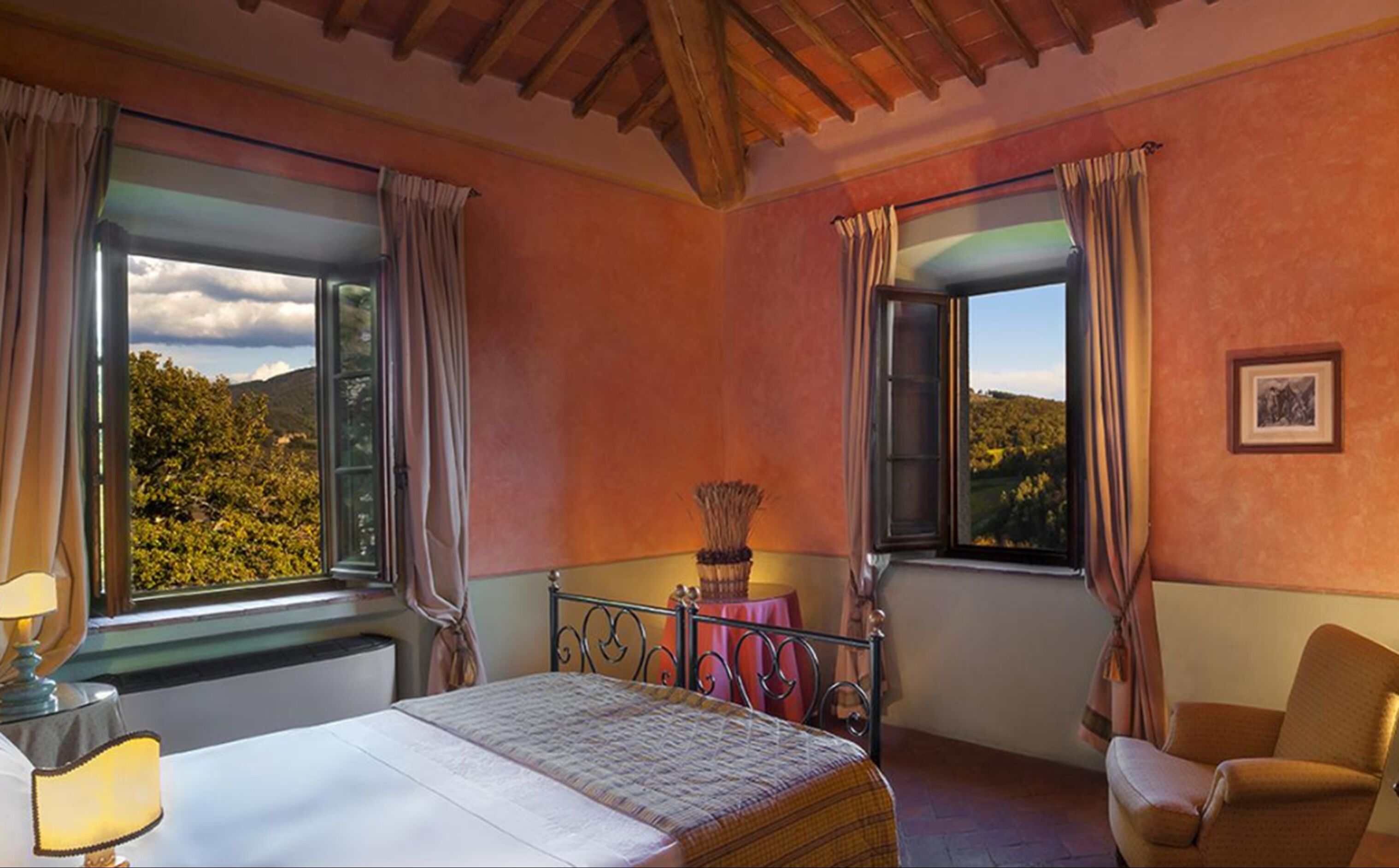 Un dormitorio con cama, una silla, un ventanal con cortinas y vistas a árboles.