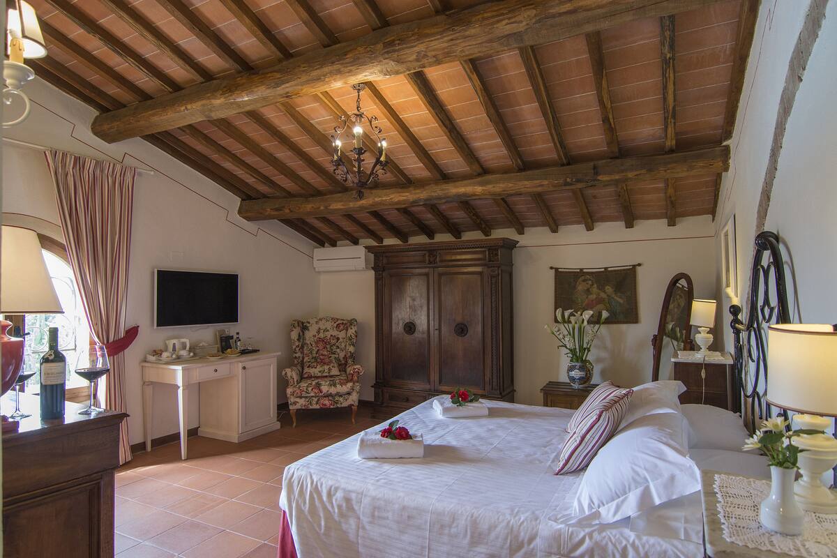 Un dormitorio con techo de madera, una cama con sábanas blancas, un escritorio con silla y un televisor en la pared.