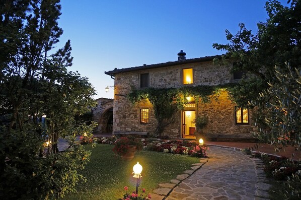 A stone building with ivy-covered walls, a stone pathway, and a garden with flowers.