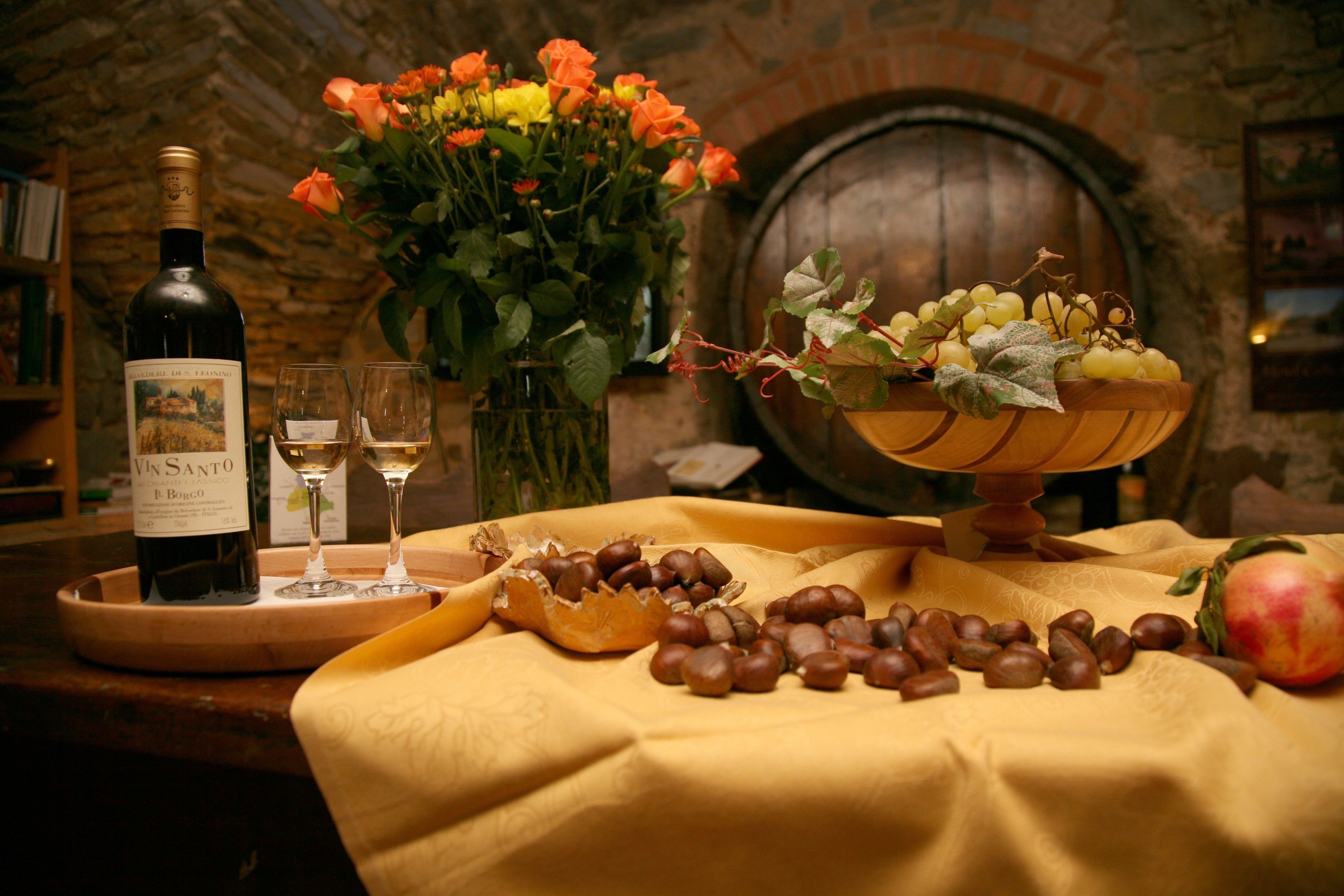 A table with a bottle of wine, glasses, a bowl of grapes, and a pomegranate.