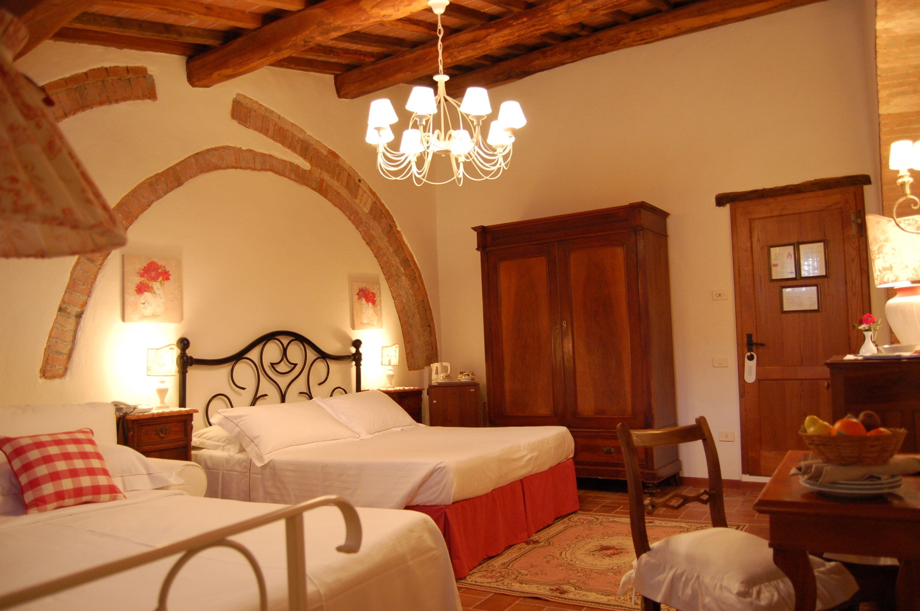 A bedroom with two beds, a chandelier, wooden furniture, and a rustic archway.