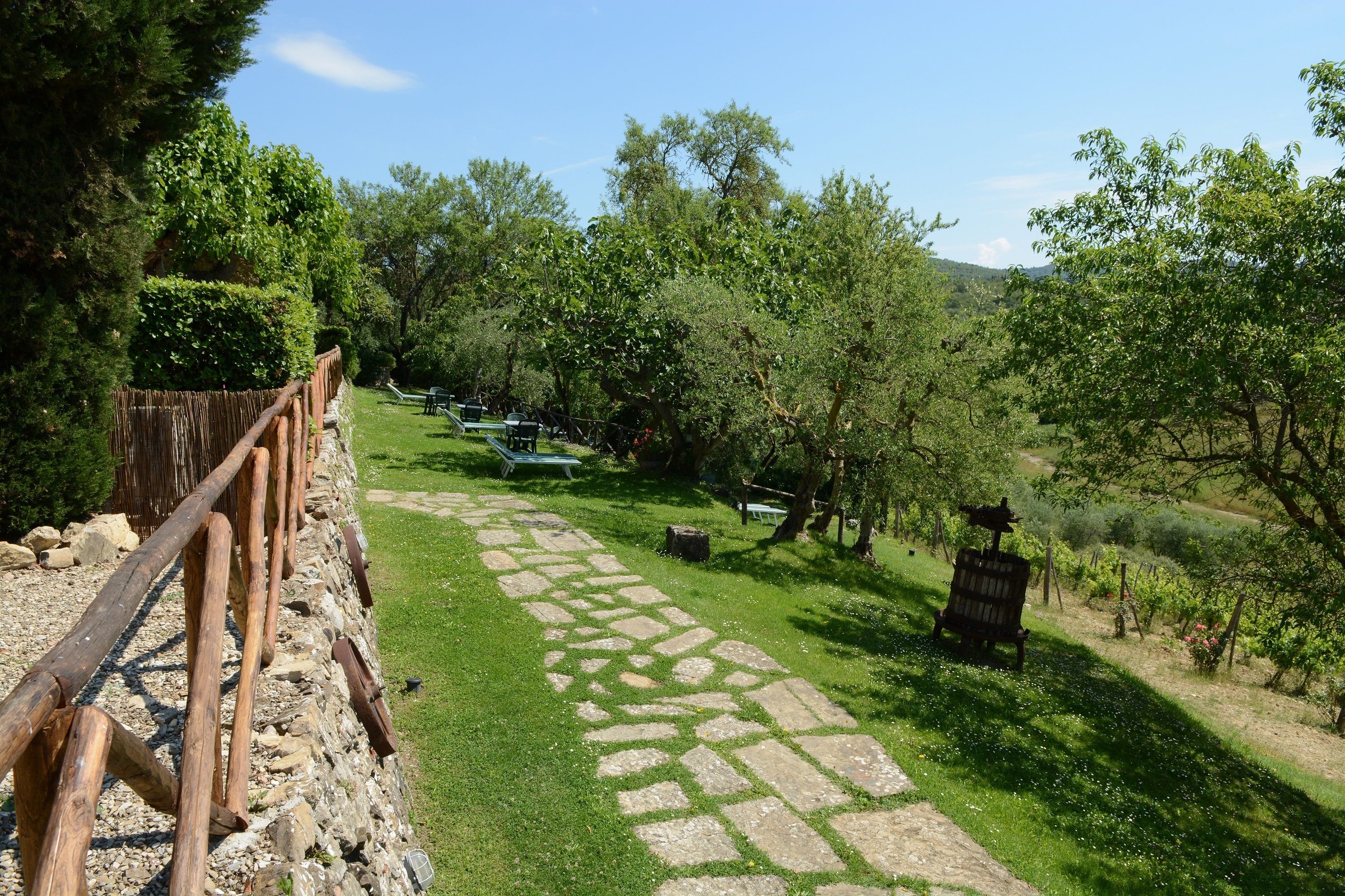 Un vialetto in pietra che si snoda attraverso un rigoglioso giardino, con una recinzione in legno su un lato e una panchina in lontananza.