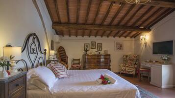 A bedroom with a large bed, wooden ceiling beams, a dresser, a chair, and a desk.