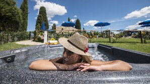 Eine Person entspannt sich in einer Badewanne mit Blick auf ein Gebäude und Bäume im Hintergrund.