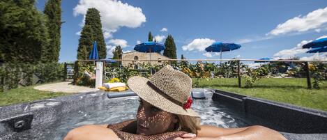 A person relaxing in a hot tub with a view of a building and trees in the background.