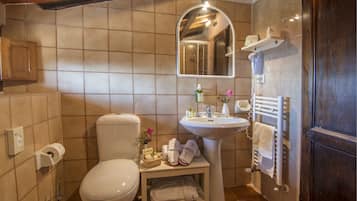 Une salle de bain avec des toilettes, un lavabo et un miroir. On y trouve un porte-serviettes et une étagère au-dessus du lavabo.