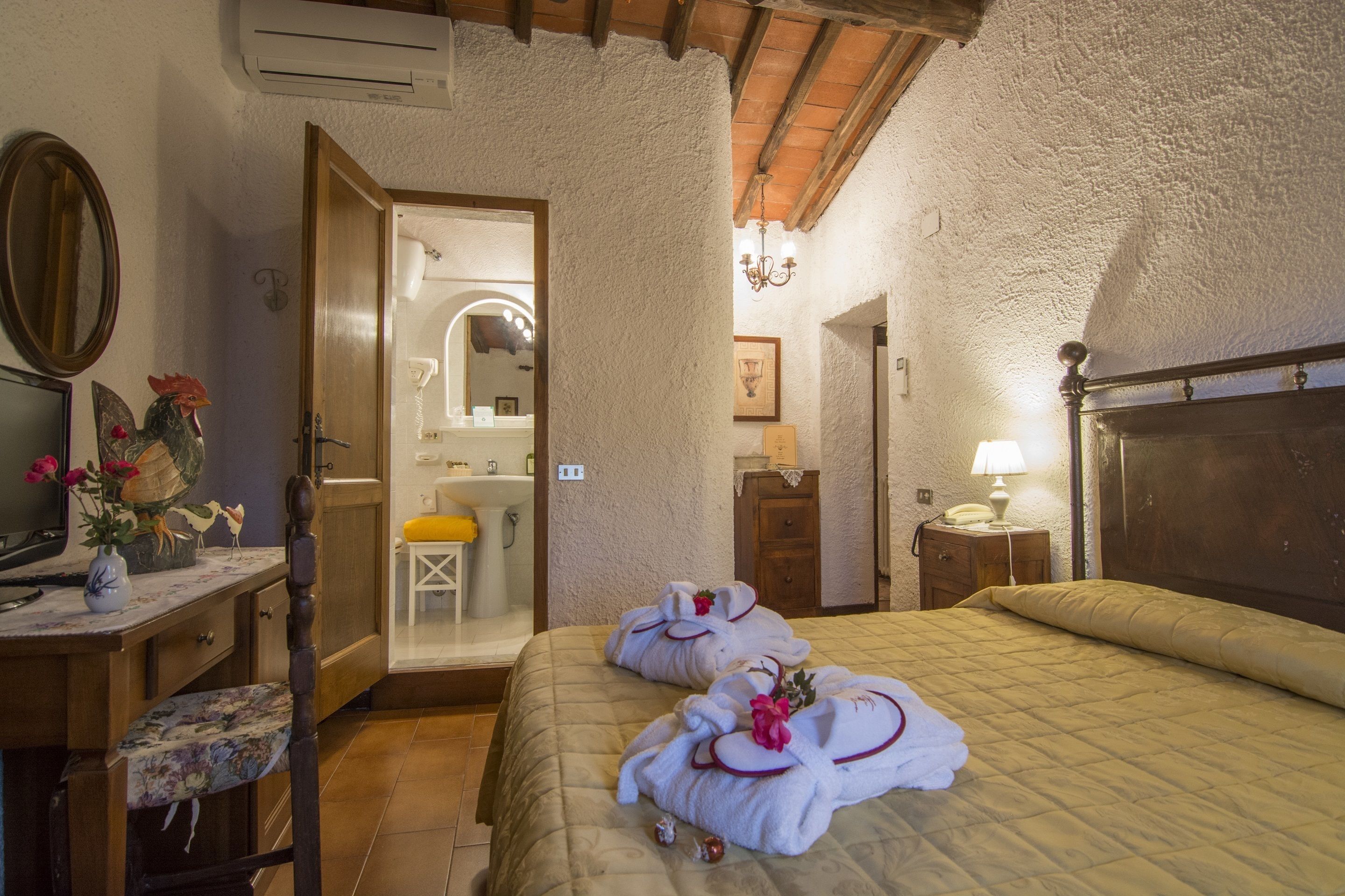 Habitación de hotel con cama, escritorio con silla, espejo y baño visible a través de una puerta abierta.