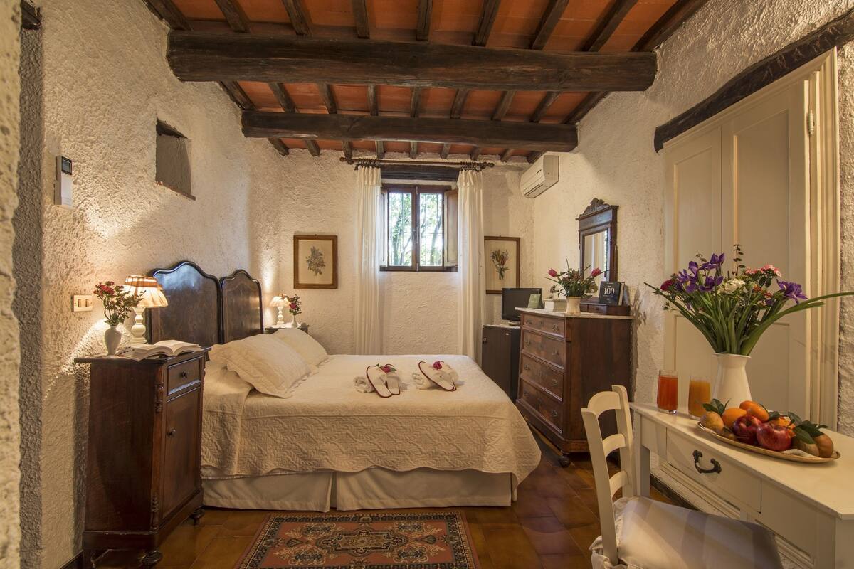 A bedroom with a wooden ceiling, a bed with white linens, a dresser, a mirror, and a window with curtains.
