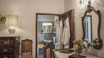 A bathroom with a wooden chair, a table with a book and vase, and a mirror with a decorative frame.