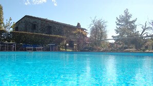 A clear blue pool with lounge chairs and a stone building in the background. - Hotel Colle Etrusco Salivolpi (Castellina in Chianti)