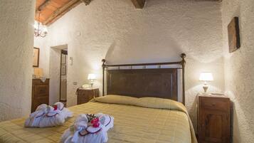 Un dormitorio acogedor con cabecera de madera, colcha acolchada y dos toallas con motivos florales sobre la cama. Hay dos mesitas de noche con lámparas y una mesita auxiliar de madera.