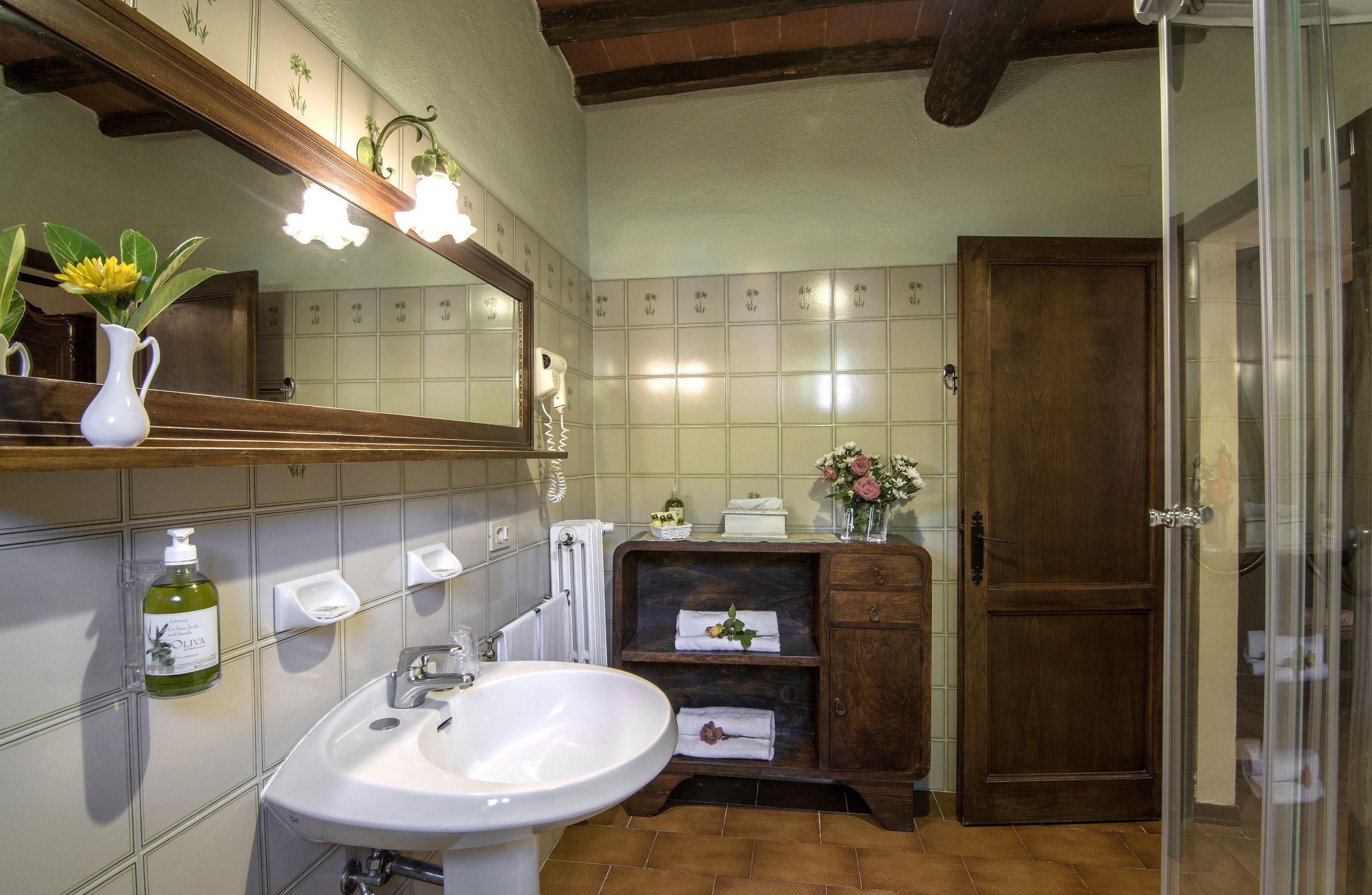 A bathroom with a white sink, a mirror, a wooden cabinet, and a shower area.