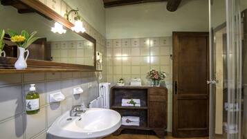 Un baño con un lavamanos blanco, un espejo, un mueble de madera y una zona de ducha.